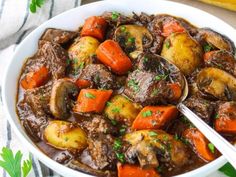 a white bowl filled with stew and carrots on top of a table next to bread