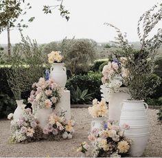 several white vases with flowers on them in the middle of a gravel ground area