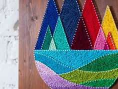 a colorful wall hanging made out of string and yarn with mountains in the middle on a wooden surface