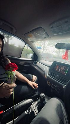 a woman sitting in the driver's seat of a car with a rose in her hand