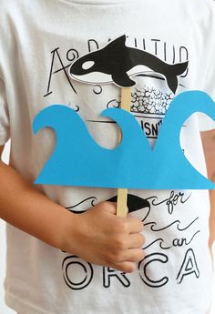 a young boy holding up a paper cut out of the shape of a wave with a dolphin on it