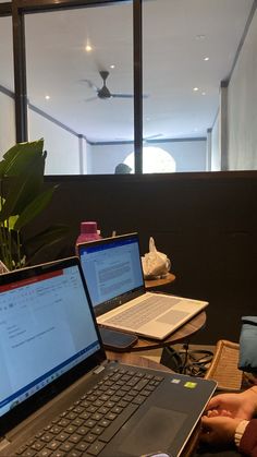 two laptop computers sitting on top of a wooden table next to a potted plant