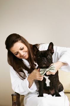 a woman sitting on a couch petting a small dog with a bow tie around its neck