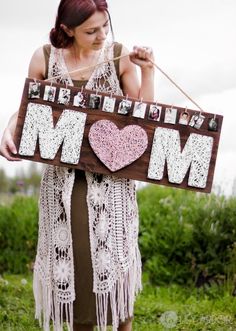 a woman holding a sign with the word mom written on it and pictures hanging from it