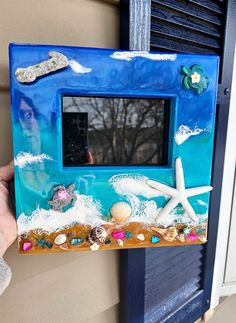 a person holding up a blue frame with seashells and starfish on it