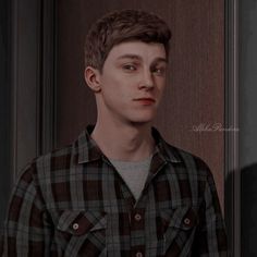 a young man standing in front of a door wearing a black and white checkered shirt