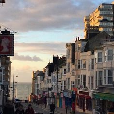 people are walking down the street in front of some buildings near the ocean and water