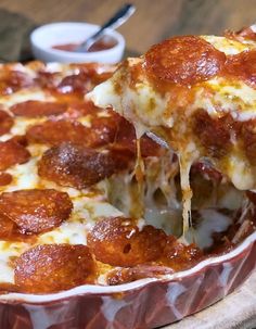 a slice of pepperoni pizza being lifted out of a pie dish with cheese and sauce