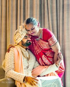 a man and woman sitting on top of a couch next to each other in front of a curtain