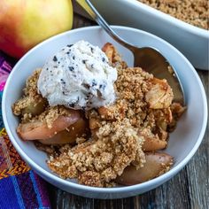 an apple crisp with ice cream in a white bowl next to another dish on a wooden table