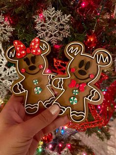 someone holding up two decorated cookies in front of a christmas tree