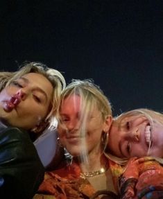 three women are posing for a photo with their faces painted red and yellow, while one woman is covering her mouth