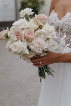 a woman holding a bouquet of white and pink flowers on her wedding day in front of a building