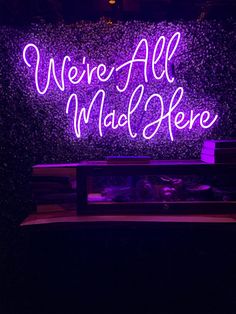 we're all mad here neon sign on display in front of a purple wall