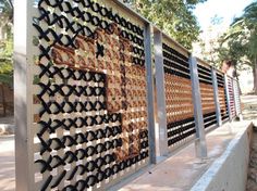 a wall made out of wine bottles on the side of a road with trees in the background