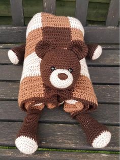 a crocheted teddy bear laying on top of a wooden bench