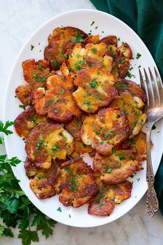 a white plate topped with potatoes covered in cheese and parsley next to a fork