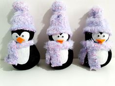 three stuffed penguins with hats and scarves are lined up against a white wall,