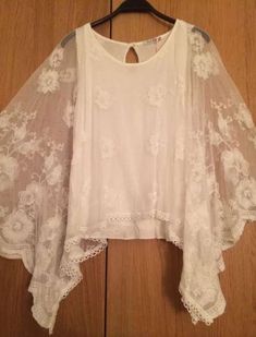 a white top is hanging up on a wooden hanger and it has lace over the shoulders