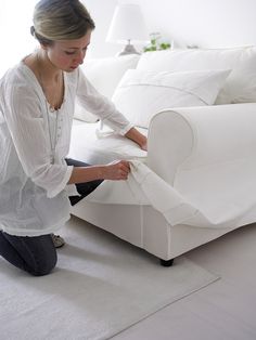 a woman kneeling on the floor next to a white couch with sheets folded over it