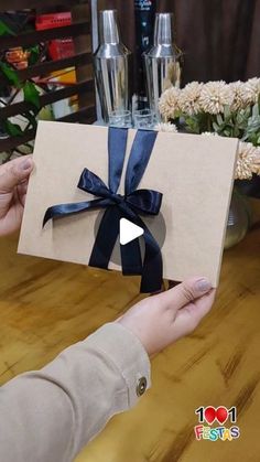 a person holding up a card with a blue ribbon on it and flowers in the background