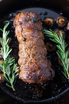 some meat in a skillet with rosemary sprigs on the side and mushrooms