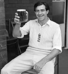 a man sitting on a stool holding up a beer mug in front of a brick wall