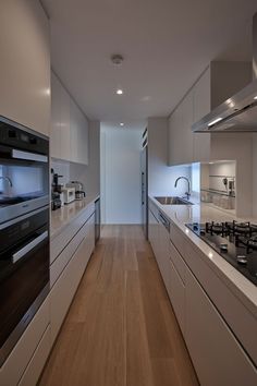 a kitchen with white cabinets and wood flooring next to a stove top oven in the middle