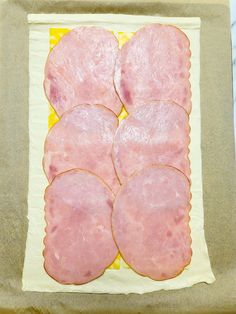 four slices of ham sitting on top of a piece of parchment paper in front of a yellow and white background