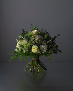 a bouquet of white flowers and greenery on a dark surface with light coming from behind