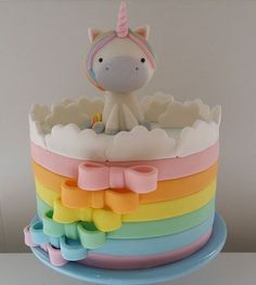 there is a cake that has a unicorn on top and rainbow ribbons around the edges