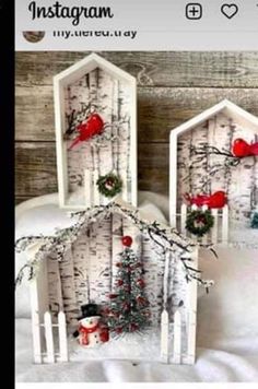 two small houses made out of white birch trees with red birds on the roof and wreaths