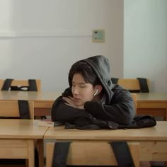 a young man sitting at a table with his head on his hands while wearing a hoodie