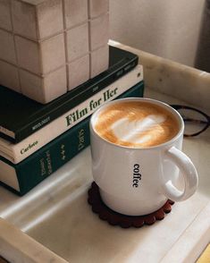 a cup of coffee sitting on top of a white tray next to two green books