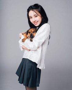 a young woman holding a small dog in her arms and smiling at the camera while standing against a gray background