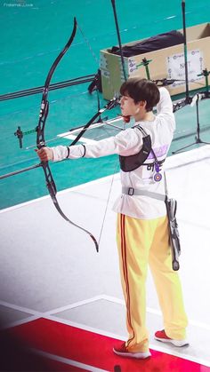 a man in yellow pants and white shirt holding a bow while standing on a stage