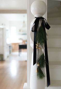 a white vase with black ribbon and bells on the top is decorated with pine branches