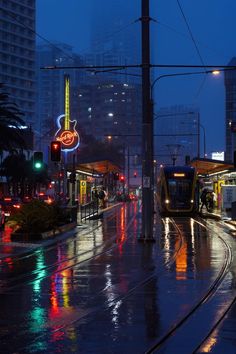 a city street at night with traffic lights and trams on the tracks in the rain