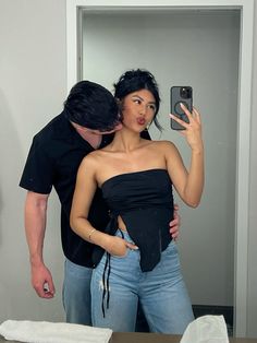 a woman taking a selfie in front of a mirror with a man looking at her