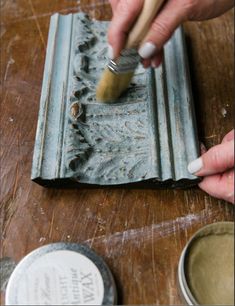 a person is painting a piece of wood on a wooden table with paint and a brush