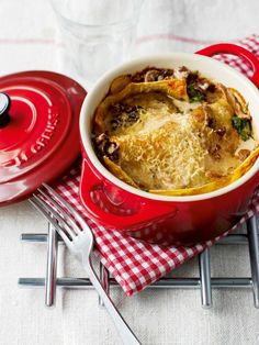 a red casserole dish with cheese and mushrooms in it on a tablecloth