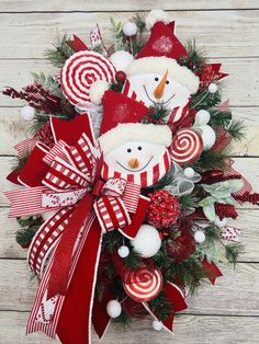 a christmas wreath with two snowmen and candy canes on the top, sitting on a wooden surface