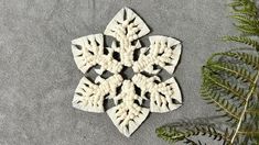 a white snowflake ornament sitting on top of a table next to a fern