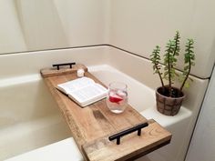 a bath tub with a wooden tray holding a book, glass of water and a potted plant