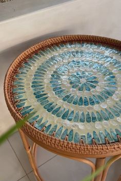 a wicker table with blue and white designs on it next to a potted plant