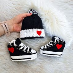 someone is holding their baby's shoes and knitted hats with hearts on them