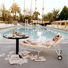 a woman laying in a chaise lounge next to a pool with newspaper on the ground