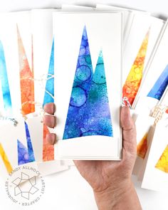 a person holding up some cards with watercolors on them and the paper is made to look like mountains