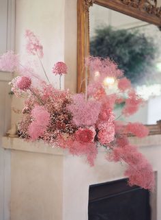 pink flowers sitting on top of a mantle in front of a mirror and fire place