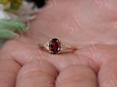 a woman's hand holding a ring with a red stone and two white diamonds